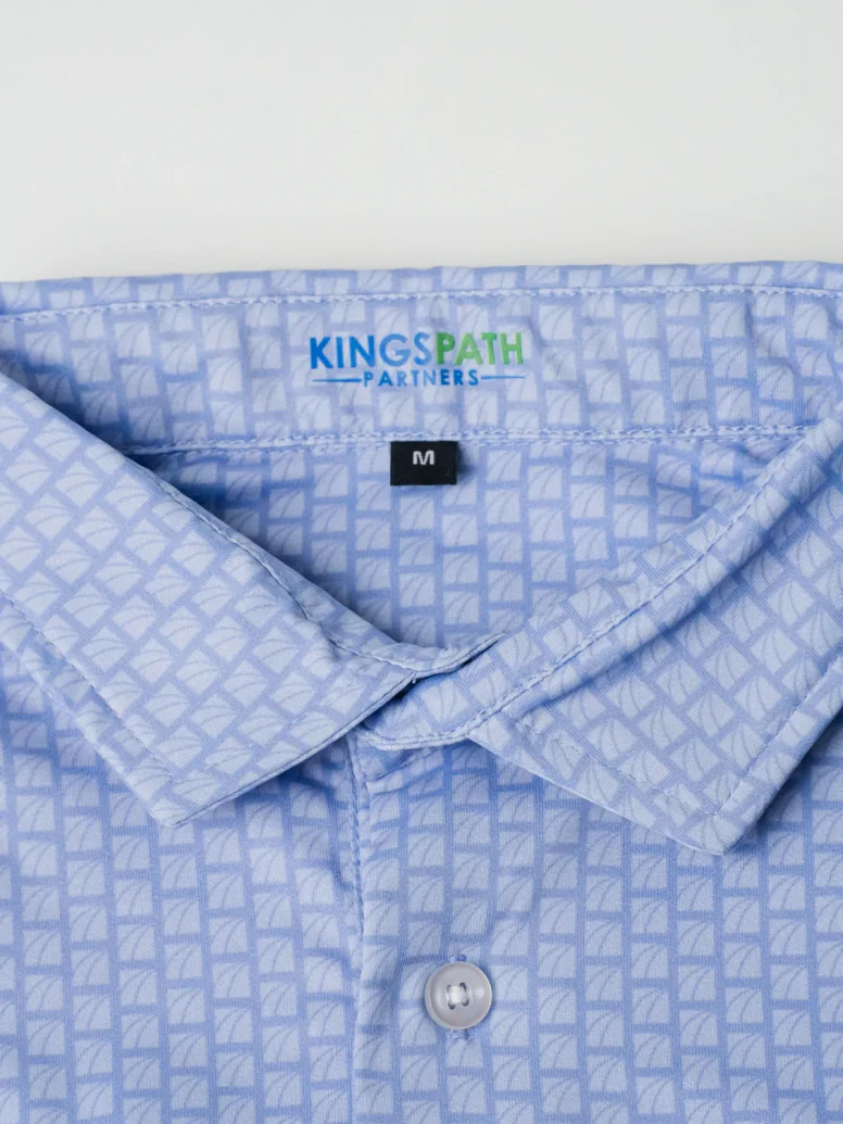 Collar of a light blue Kingspath Partners polo with a tonal logo micro print
