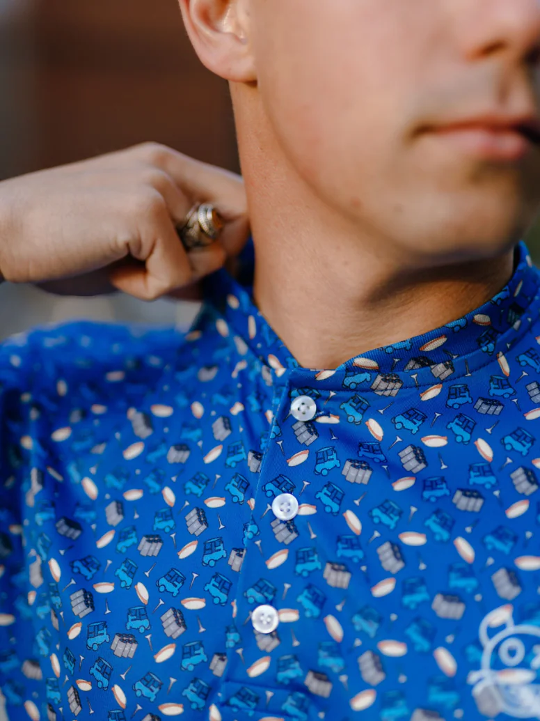 Close view of the collar of a blue polo with a repeating icon pattern, held by one hand