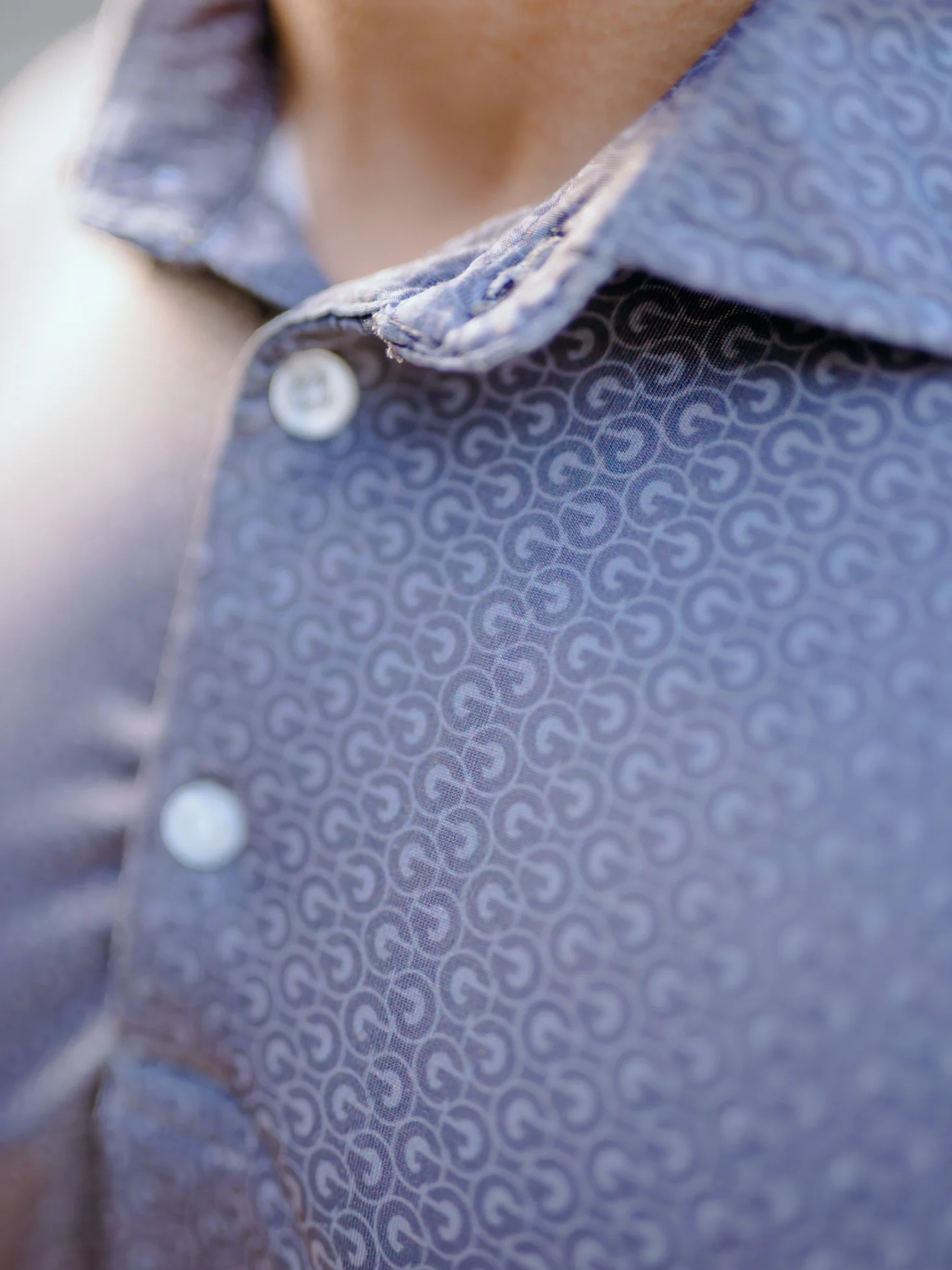 Close view of the collar and placket of a navy polo with a tonal logo pattern