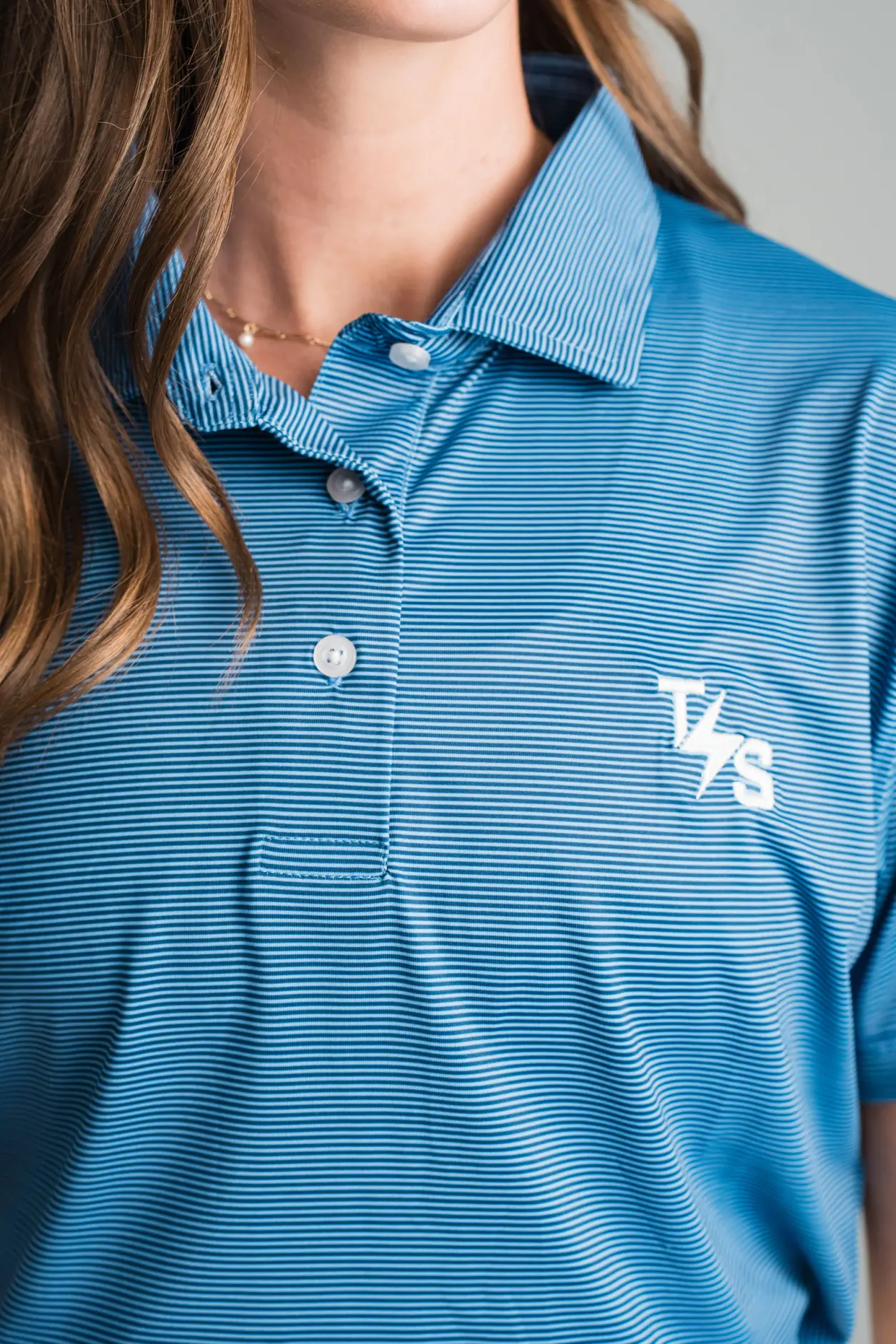Close view of a blue striped TechServ polo with a white embroidered logo