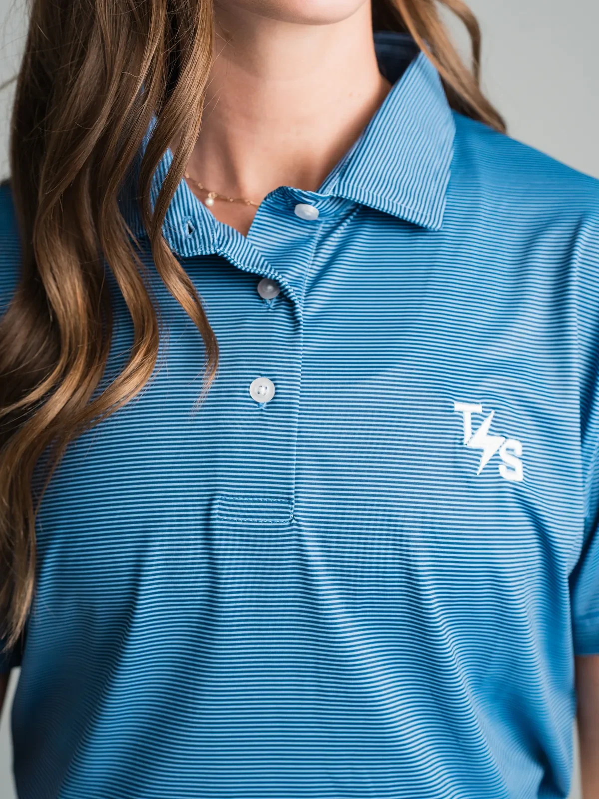 Woman wearing a blue striped custom polo with an embroidered logo for custom apparel vs name-brand corporate programs