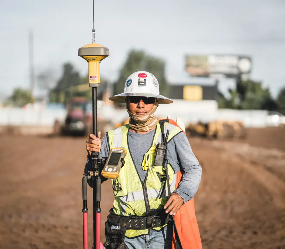 Surveyor in a safety vest holding equipment at a jobsite