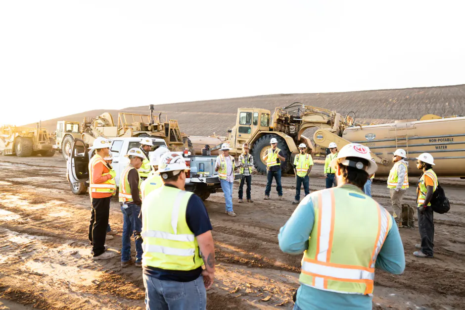 Construction workers in safety vests meeting beside heavy equipment