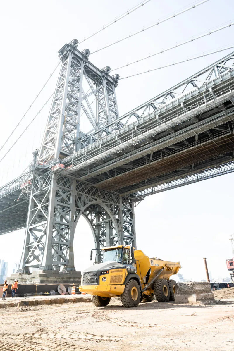Yellow construction vehicle beneath a steel bridge