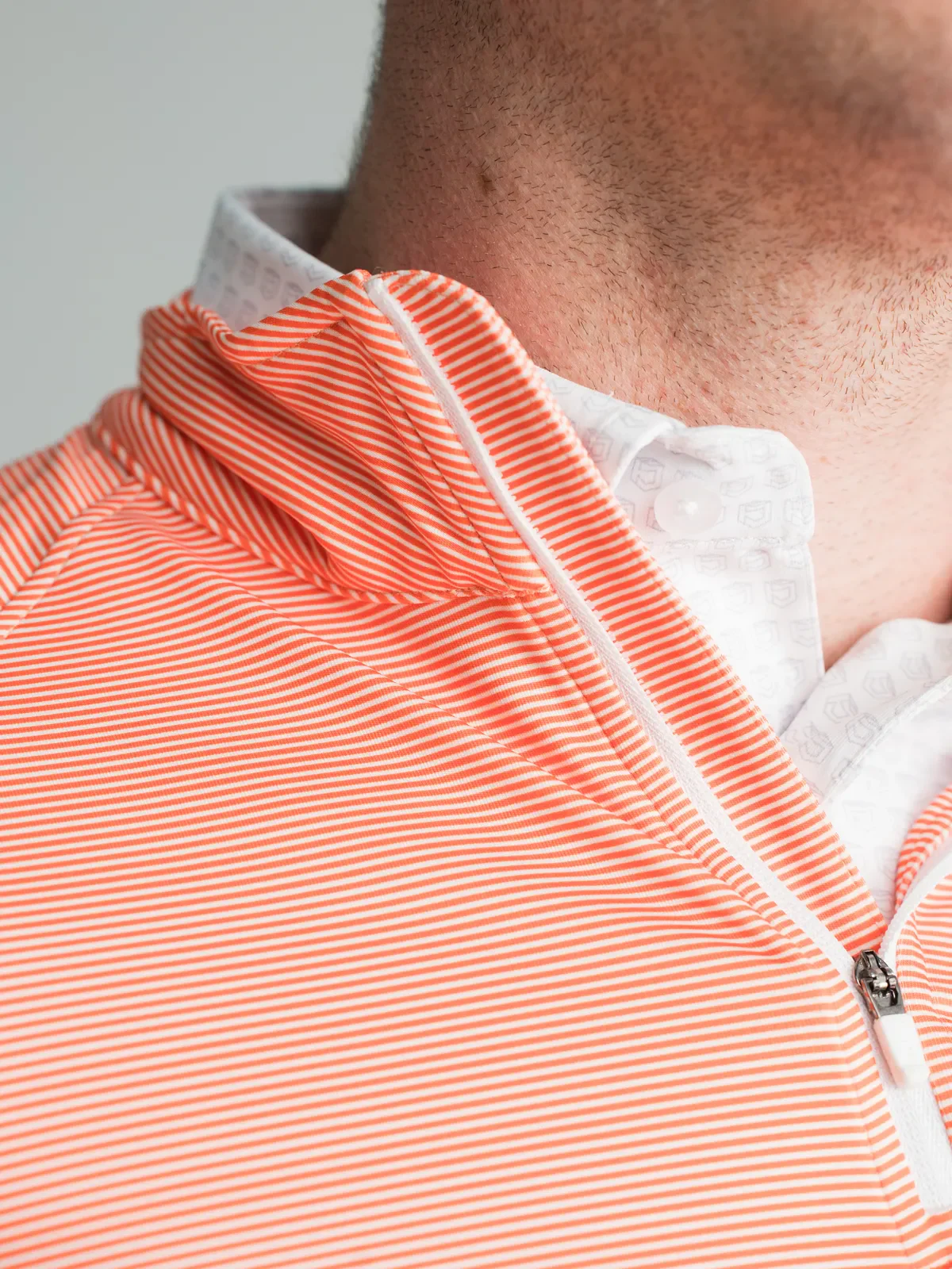 Close view of a coral striped quarter zip collar over a white patterned polo