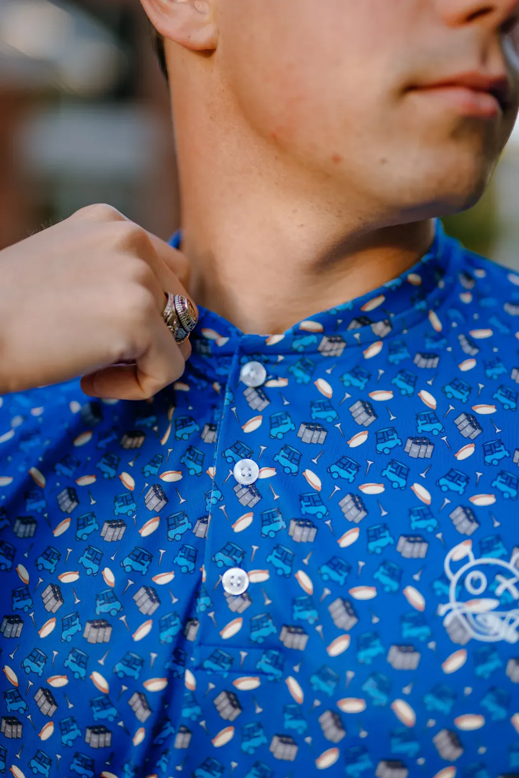 Man adjusting the collar of a blue custom polo with a golf cart pattern